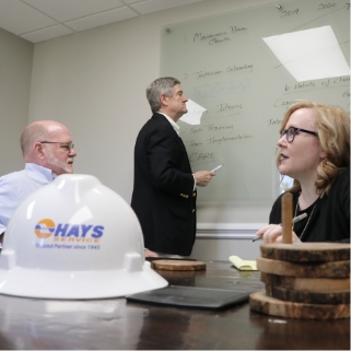 hays employees sitting at round table with whiteboard behind having a discussion