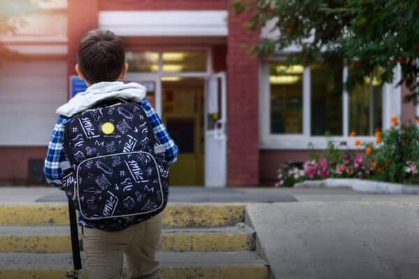 Young boy wearing a backpack and walking toward the school building.