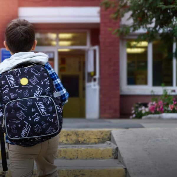 Young boy wearing a backpack and walking toward the school building.